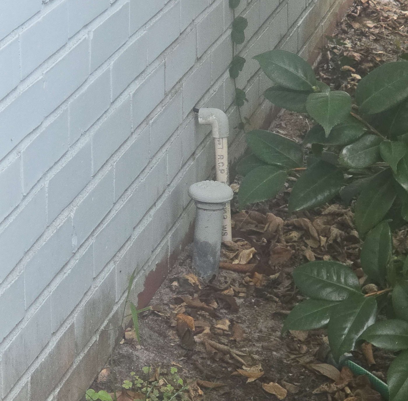 Capped vent pipe at the soil line beside a home's exterior wall — the visible evidence of a buried fuel-oil tank